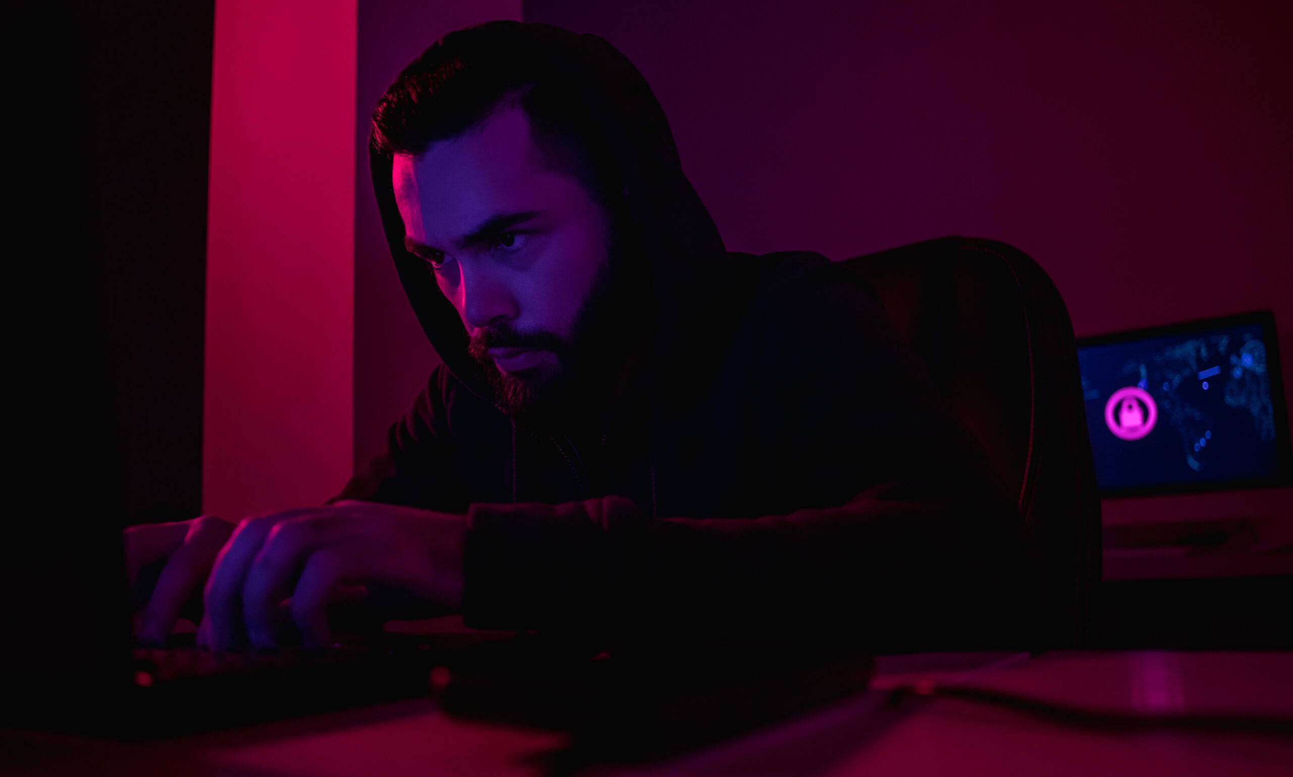 Online extortion is on the rise in Ontario and Richmond Hill Affordable Criminal Lawyer Plug are seeing this too. Serious bearded guy in hoodie using laptop to extort money through Internet while sitting in dark room
