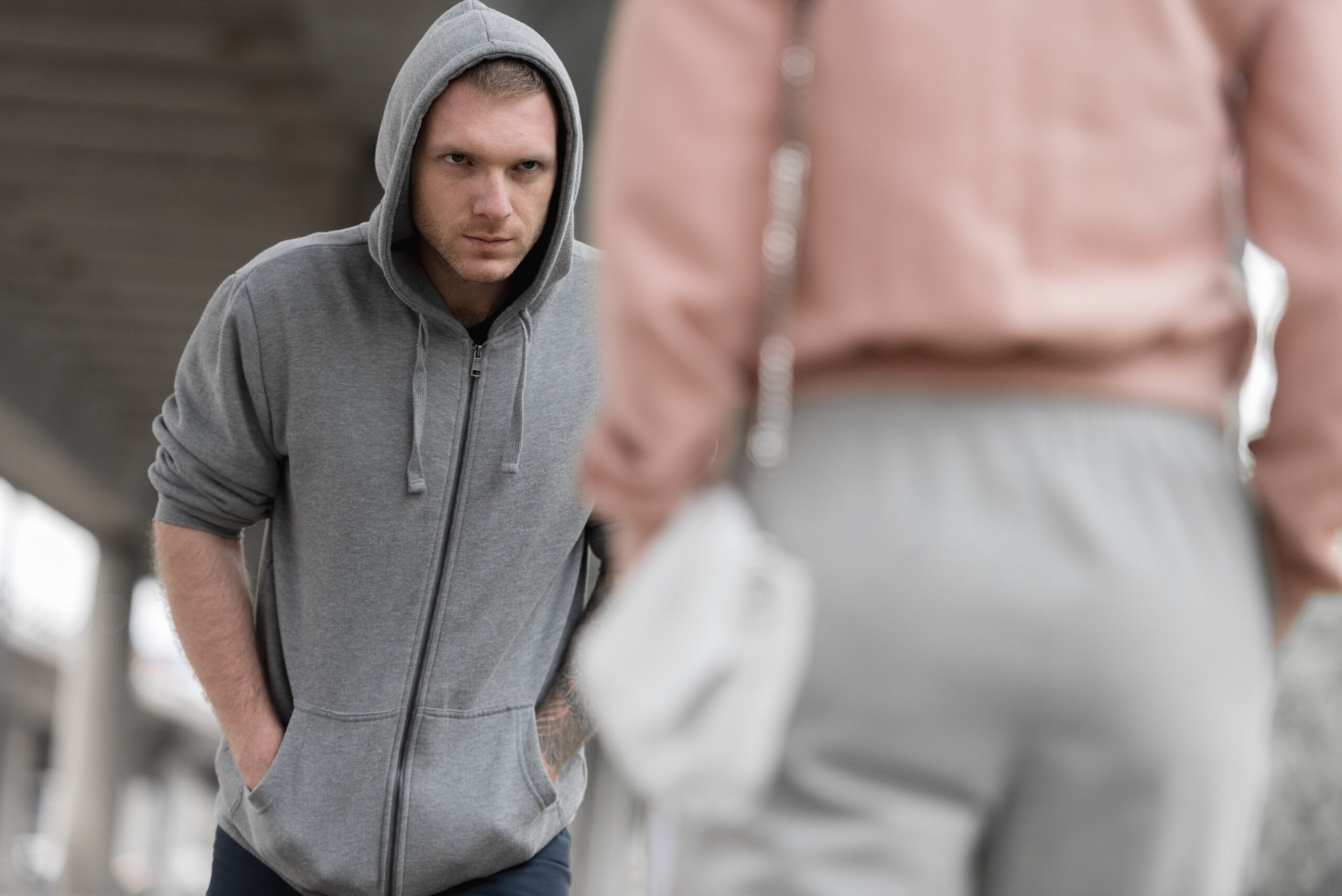 young male robber in hoodie going to steal handbag from woman