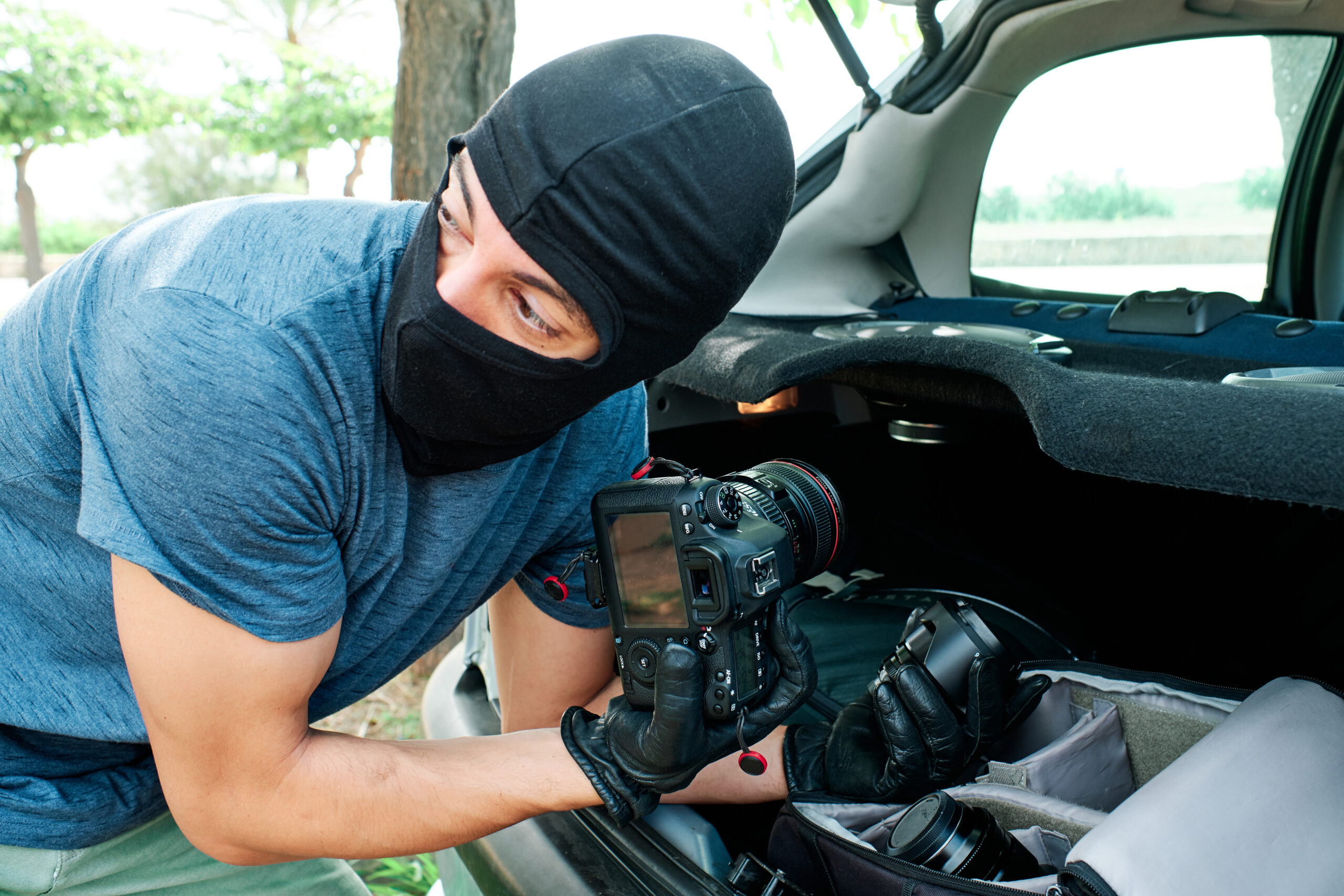 a thief with a mask stealing photography equipment and lenses from a car - Insurance and legal concept